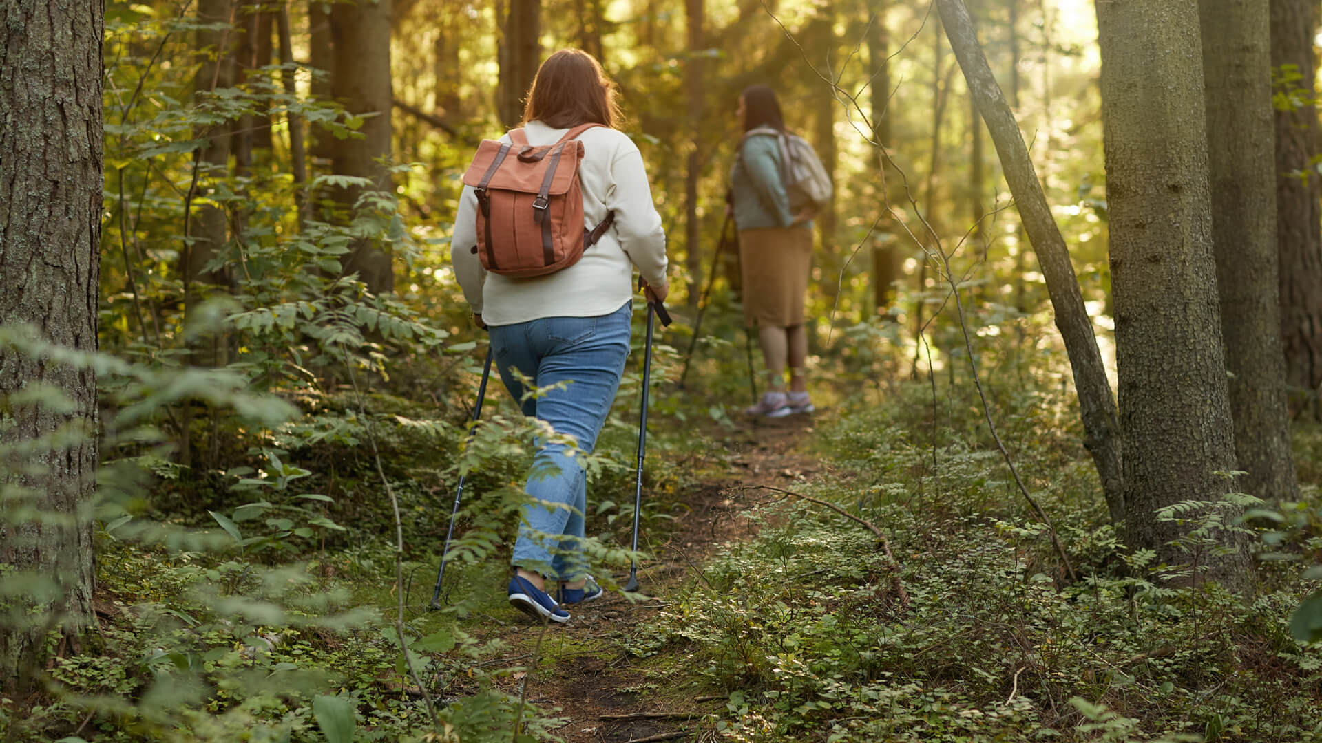 Two hikers with backpacks trekking through a lush forest.
