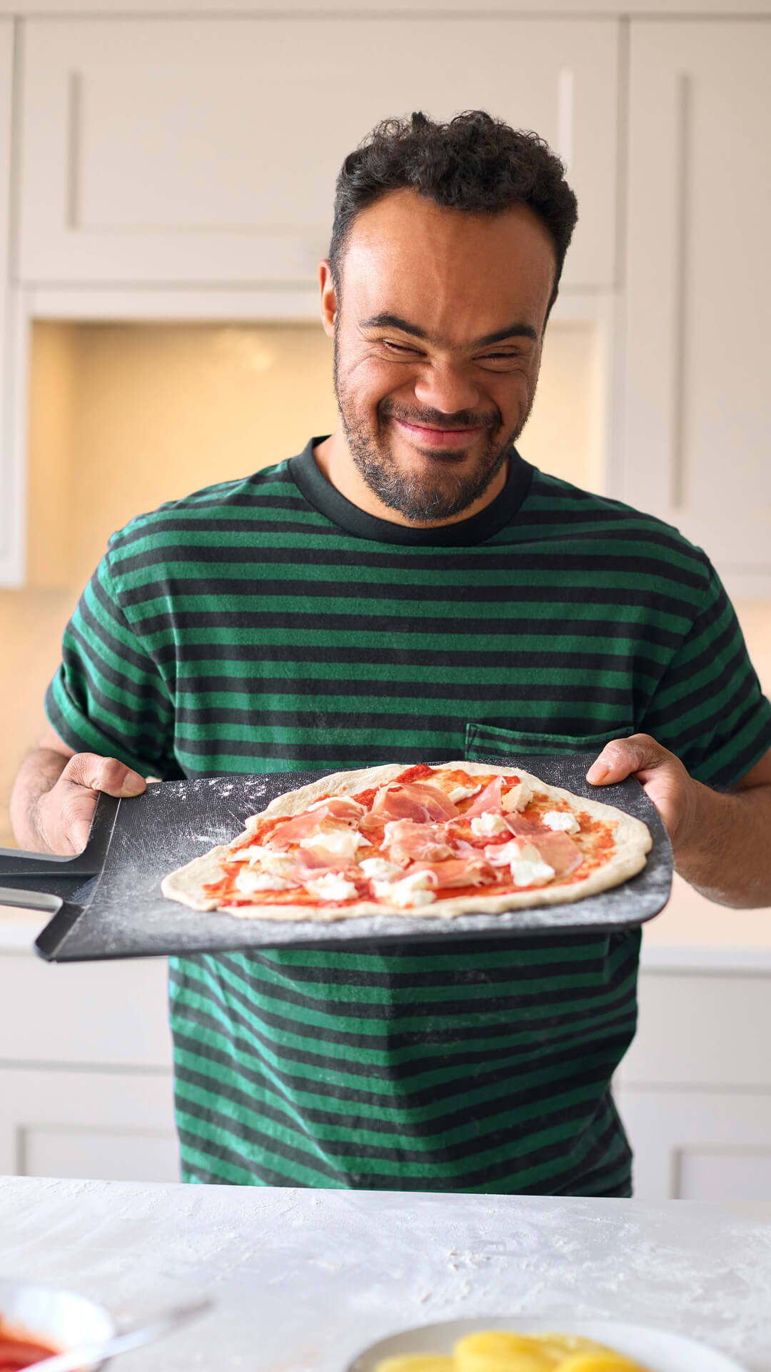 Man with pizza smiles in kitchen.